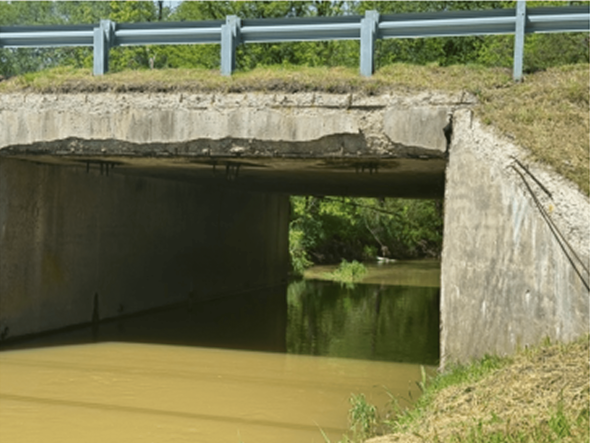 Concrete bridge over a muddy river with greenery around.