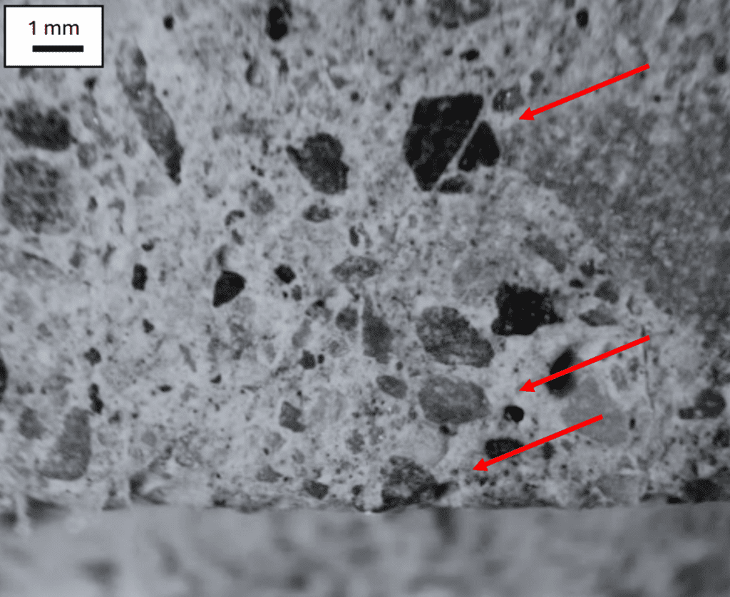 Microscopic image showing black particles with red arrows pointing at specific areas.