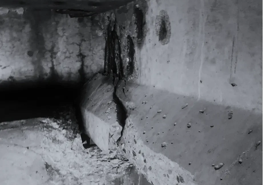Close-up of a cracked, weathered concrete surface in a dimly lit area.