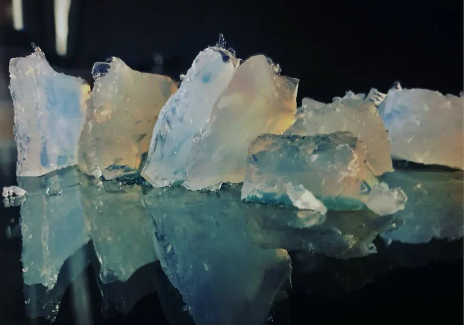 Close-up of translucent crystals with blue and clear hues on a reflective surface.