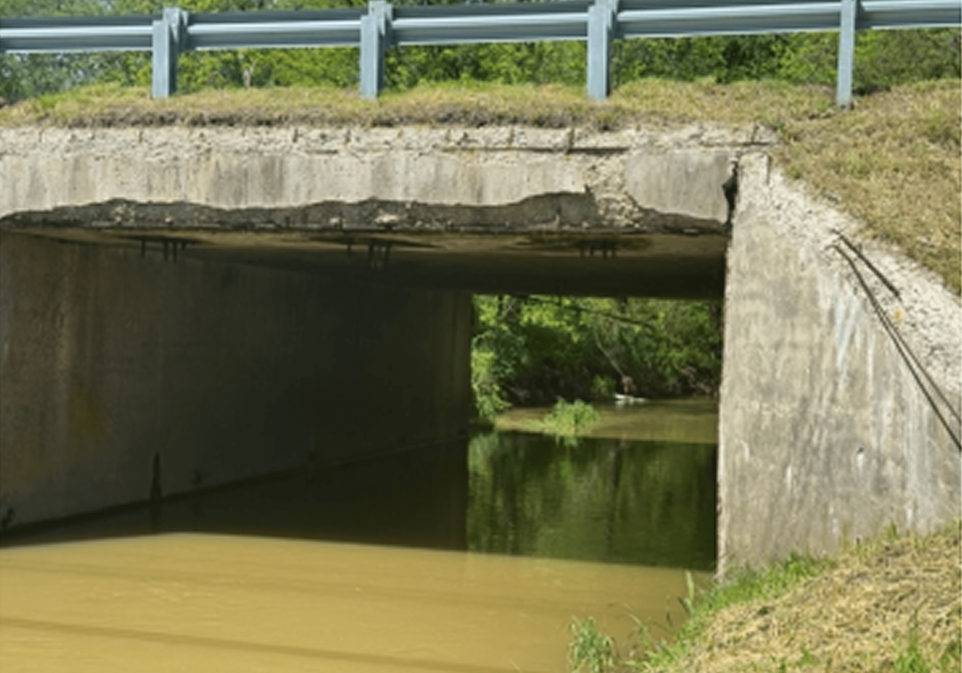 Concrete bridge over a muddy river with greenery around.